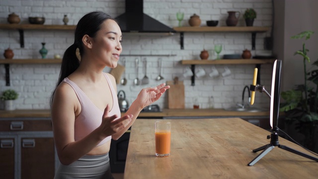 健康的亚洲女性在智能手机上用LED环灯直播视频，手里拿着新鲜的果汁。植入式广告的概念