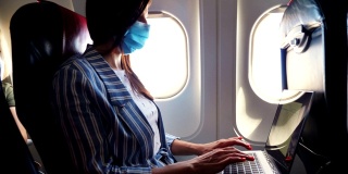 在一架飞机的机舱里，一个戴着防护面具的年轻女子，一名自由职业者在一台笔记本电脑上工作。工作和旅行的概念。新冠肺炎疫情后航班开通