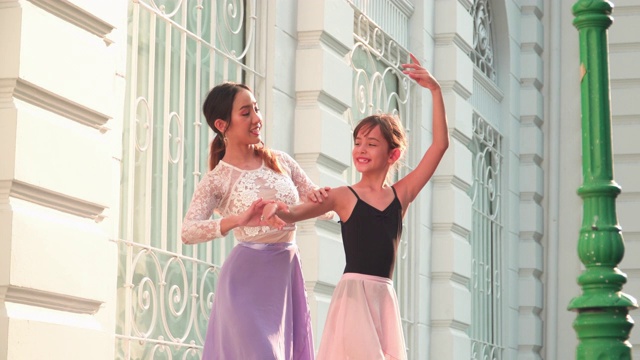 在一个阳光明媚的日子里，一名亚洲青少年芭蕾舞演员在一名年轻女芭蕾舞老师的建议下，在泰国曼谷当地的街道上练习芭蕾舞。活跃的年轻妇女和孩子的概念周末活动和当地地标。