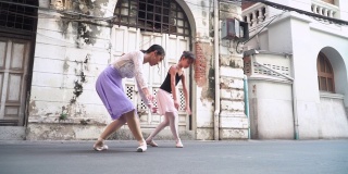 低视角:在泰国曼谷的街道上，一名亚洲芭蕾舞少女正在练习芭蕾舞，动作与年轻女芭蕾舞老师的动作相同。概念上的活跃的年轻妇女和孩子在周末的活动和当地的地标。