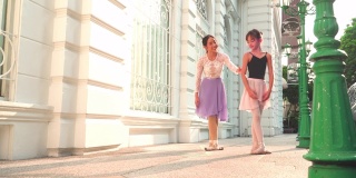 低角度视角:在一个阳光明媚的日子里，一名亚洲青少年芭蕾舞演员在一位年轻女芭蕾舞老师的建议下，在曼谷当地的街道上练习芭蕾舞。活跃的年轻妇女和孩子的概念周末活动和当地地标。