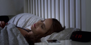 因为电话留言而醒来。年轻女子躺在床上，被手机吵醒了。