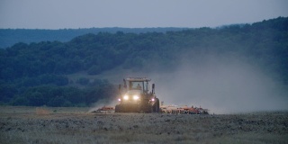 工作到很晚。在犁地。在收获季节结束时，拖拉机在油菜地里工作，夜间开着前灯犁地。农业职业。