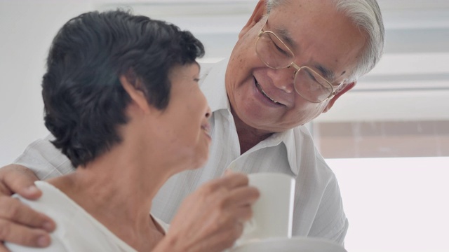 亚洲老男人拿着咖啡杯在早上给他的妻子。幸福的亚洲老夫妇花时间与家人在家里。高级的肖像