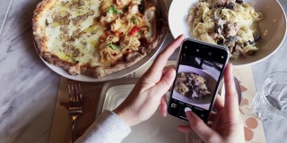 一名女博主用智能手机拍摄美食，在意大利餐厅拍意大利面和披萨，并在网上发布社交媒体生活方式