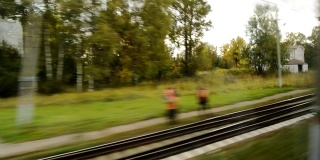 从一列行驶的火车的窗口看过去，快速移动的一个小村庄，一个十字路口，一个车站，黄色的树木在一个多云的秋天的一天
