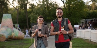 一对时髦的夫妇在城市公园散步吃着冰淇淋和华夫饼开怀大笑。浪漫的年轻男女在户外享受他们的闲暇时光。男朋友和女朋友的慢动作