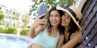 两名身穿比基尼泳装的亚洲女性在游泳池前自拍和拍照。积极情绪与慢动作。