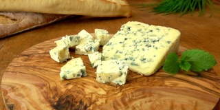 蓝色的羊乳酪放在一块木板上，背景是法式长棍面包