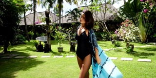 美丽的年轻亚洲女人穿着比基尼和夏季海滩和服或帕雷奥纱笼在热带花园。暑假