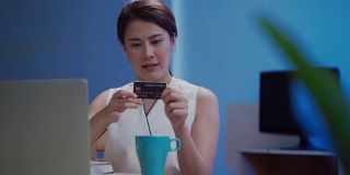 快乐的亚洲女人使用笔记本电脑和信用卡在晚上网上购物
