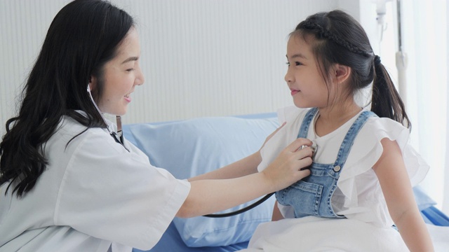 一位女医生用听诊器检查女孩听快乐健康可爱的小女孩在医院看病。