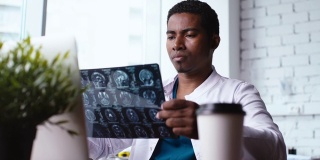 近距离观察非裔美国黑人医生在书桌上检查核磁共振脑部扫描图像。