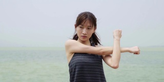 年轻的亚洲女子在海滩上伸展手臂