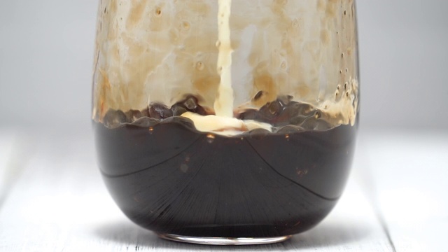 泡奶茶，将牛奶和茶倒入红糖图案的水杯中，放置在白色的木桌背景上