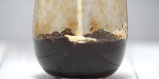 泡奶茶，将牛奶和茶倒入红糖图案的水杯中，放置在白色的木桌背景上