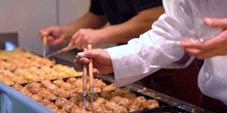在日本的街头小吃市场上，大厨在夏季的节日期间，用高清慢镜头近距离拍摄的日本小吃章鱼烧。男子烹饪什锦传统日本肉丸。