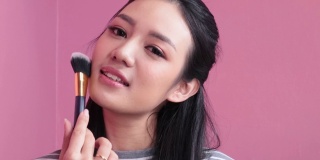女人化妆。一位年轻的亚洲女子用化妆刷在脸上刷腮红。化妆品的概念