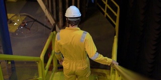 在工业环境、石油平台或液化气厂，身着黄色工作服、眼镜和头盔的年轻人。Slowmotion拍摄