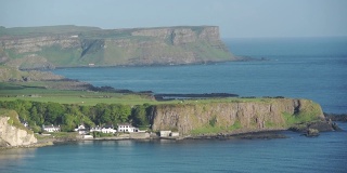 令人惊叹的风景郁郁葱葱的悬崖和美丽的房子在安特里姆海岸，爱尔兰被平静的蓝色海洋包围-宽镜头