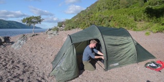 夏日里，一名游客在苏格兰喀里多尼亚运河的沙滩上搭建帐篷。采用针
