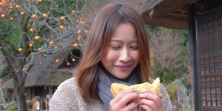 微笑的年轻亚洲女性游客喜欢吃传统的日本糕点与甜红豆沙在秋天日本古老的村庄。日本旅游和季节变化的概念。