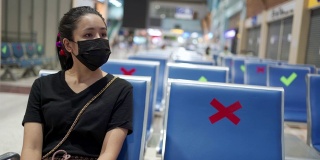 亚洲女性戴着黑色面具，独自坐着，社交距离概念，空荡荡的商场，两米距离，新常态的新冠肺炎大流行。室内大厅终端，公共场所，等待朋友