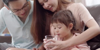 亚洲母亲给她的小女儿一杯牛奶。一个可爱的蹒跚学步的小女孩喝着牛奶。