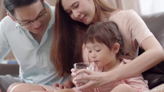 亚洲母亲给她的小女儿一杯牛奶。一个可爱的蹒跚学步的小女孩喝着牛奶。视频素材模板下载
