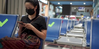 亚洲妇女戴着黑色面罩坐在椅子上使用智能手机