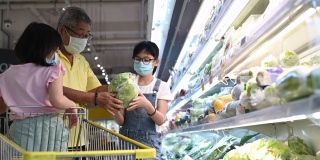 一个亚裔中国女孩和她的祖父和妹妹在超市的冷藏区买一些蔬菜