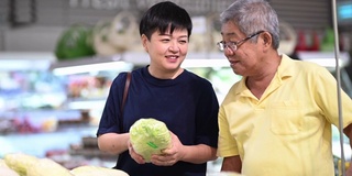 一个活跃的亚洲华人老人和他的女儿在购物和选择卷心菜