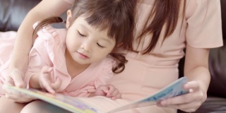 可爱的亚洲小女孩和她的妈妈在家里看书。