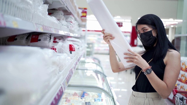 年轻的亚洲妇女戴着黑色面罩在零售批发杂货店挑选商品，人们的经济问题，信用卡债务冠状病毒新冠病毒大流行，预算生活消费习惯上的销售