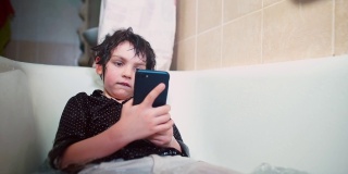 男孩躺在浴室里用手机心理困难时期的青少年