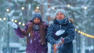 一对穿着夹克和帽子的有趣夫妇在冬天的公园里扔雪视频素材模板下载