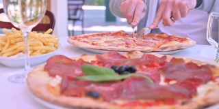 意大利餐厅的两个大披萨，里面有意大利熏火腿、罗勒和马苏里拉奶酪。传统的意大利北部薄披萨和酒在桌上。家庭午餐。有些物体焦点模糊了。