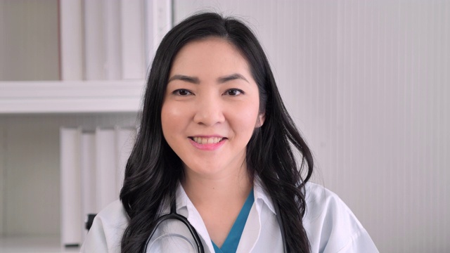 亚洲女医生经验丰富的医生自信的微笑，而看着相机摆姿势在医疗诊所单独。女医生在看视频会议。骄傲在工作