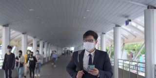 4K亚洲商务人士办公室人员走在城市火车站，使用智能手机和互联网为公司工作。商人戴口罩保护covid-19病毒大流行和空气污染。新标准的概念。