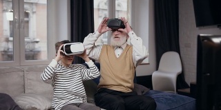 好看的正面两代人作为爷爷和孙子使用虚拟现实耳机玩电子游戏