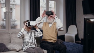 好看的正面两代人作为爷爷和孙子使用虚拟现实耳机玩电子游戏视频素材模板下载