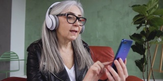慢动作的快乐好看时髦的退休妇女耳机坐在扶手椅上，听着美丽的歌曲