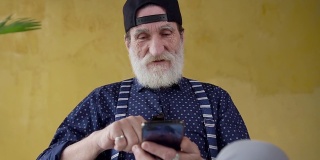 慢动作的快乐英俊的胡子时髦的男人戴着年轻的帽子，用他的智能手机搜索所需的信息