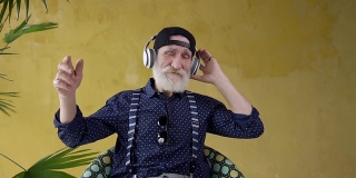 英俊潇洒的留着胡子的70岁男子戴着耳机听着美妙的音乐，看着相机