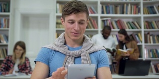 可爱的整洁开朗的现代家伙坐在大学图书馆里，用i-pad搜索需要的信息来完成家庭任务