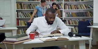 迷人的、集中的、留胡子的年轻非洲裔美国学生坐在图书馆里完成家庭作业