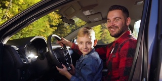 满意的35岁的胡子父亲和可爱的微笑男孩坐在掌舵和摆姿势在驾驶课上