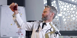 近距离观察可爱的高技能的灰色头发的男性医生，穿着白色长袍和听诊器探索在试管中的化学物质的状态
