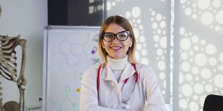 年轻女医生戴眼镜和白大褂与听诊器在颈部微笑在医院的办公室。37、医生养生，爱医医