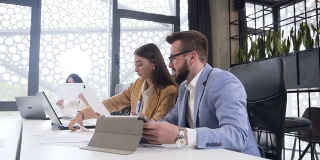 有魅力的长头发的女人和胡子的男人一起工作在商业团队，比较数据从文件报告和笔记本电脑在会议室